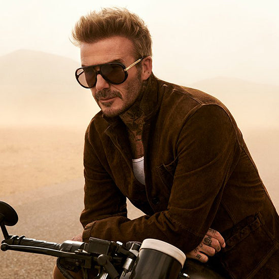 Uomo con giacca scamosciata marrone e occhiali da sole stile aviator vintage su una moto, collezione eyewear David Beckham su giarre.com.