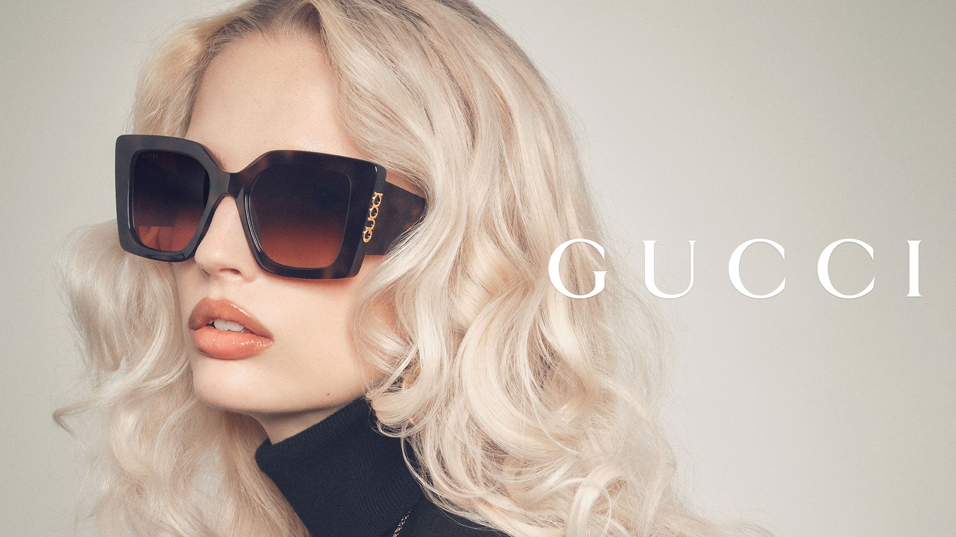 Primo piano di una donna che indossa occhiali da sole Gucci oversize con montatura tartarugata e lenti sfumate marroni. Il design audace e raffinato valorizza il look glamour, esprimendo l'eleganza e l'esclusività tipiche dell'eyewear Gucci.