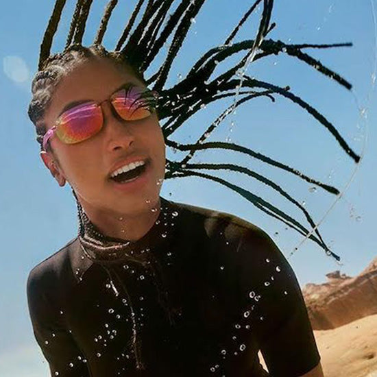 Ragazza in spiaggia di ritorno dal surf indossa occhiali da sole Maui Jim, con montatura elegante e lenti polarizzate.