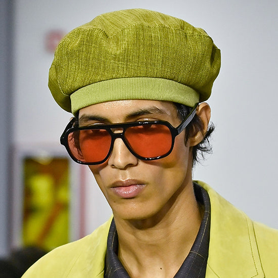Modello uomo in sfilata con occhiali da sole Paul Smith squadrati neri con lenti arancioni e cappello verde olivastro - Collezione Giarre.com